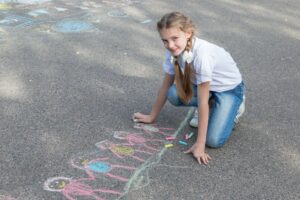 Caucasian teenager girl draws a family of little men with chalk on the asphalt