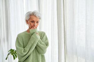 Woman with gray hair nervously bites her nails at the window