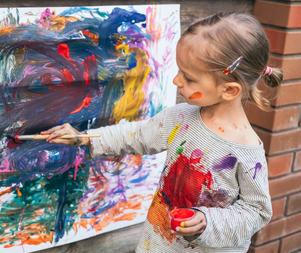 Beautiful little girl painting with various colors on paper, close-up. Art therapy concept